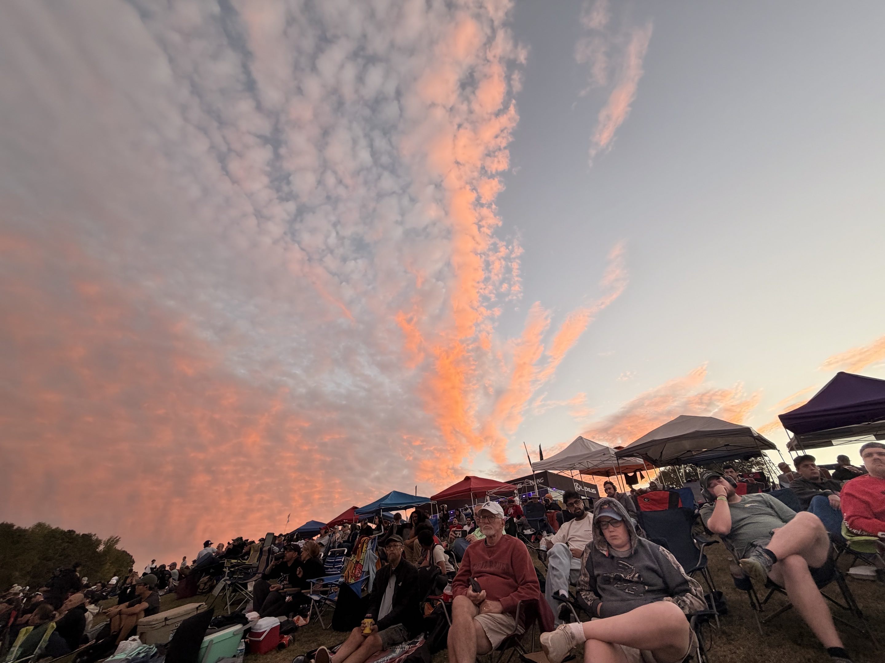 Gorgeous clouds at sunset over a hill covered with people watching a motor race